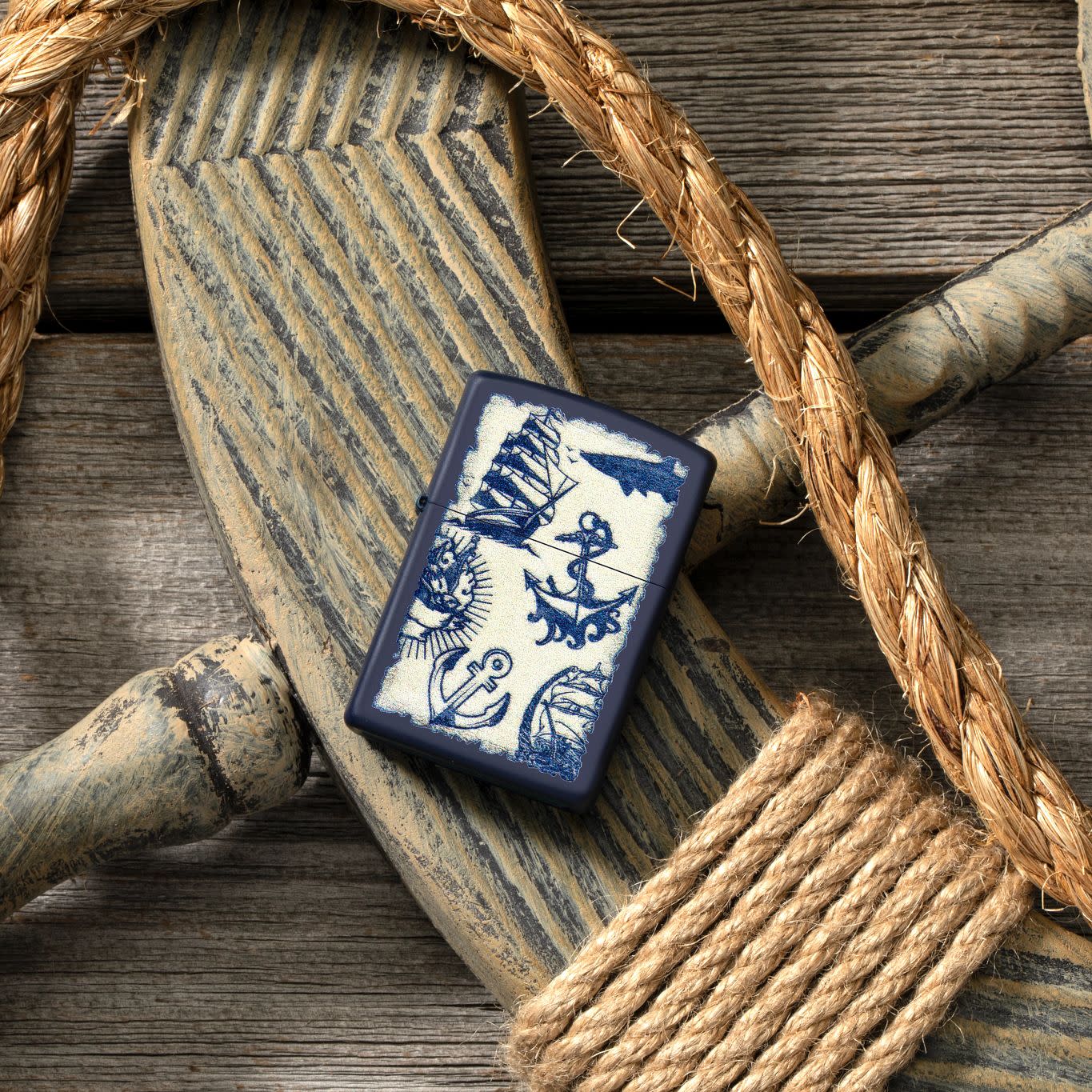 Lifestyle image of Nautical Design Navy Matte Windproof Lighter laying on a ship's helm with rope around it.