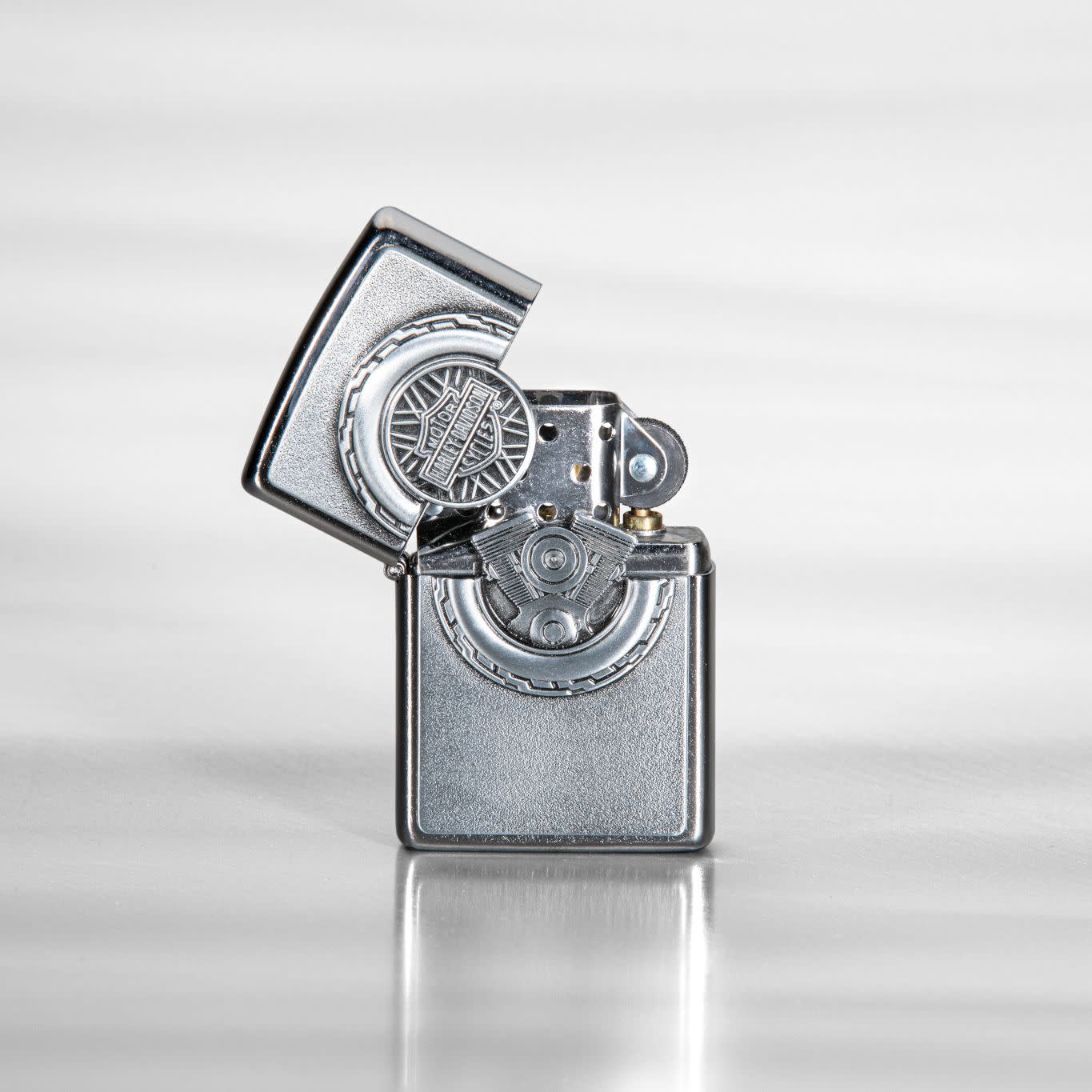 Lifestyle image of Harley-Davidson® Engine Surprise Emblem Street Chrome Lighter, standing on a reflective metal sheet